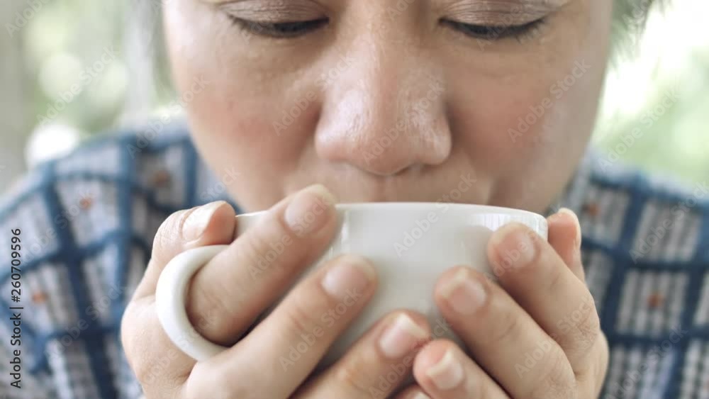 Middle-aged asian woman sitting in a cafe with a Cup of tea or coffee and swallowing. Close-up of hands with a Cup Middle-aged asian woman sitting in a cafe with a Cup of tea or coffee and swallowing. Close-up of hands with a Cup