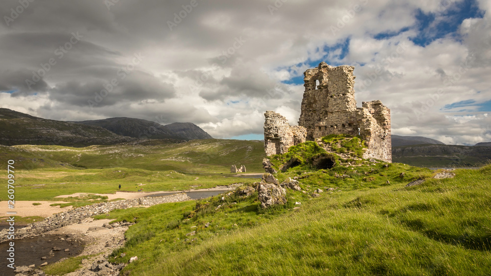 Ardvreck Castle in Scotland on a green hill under blue sky with white clouds