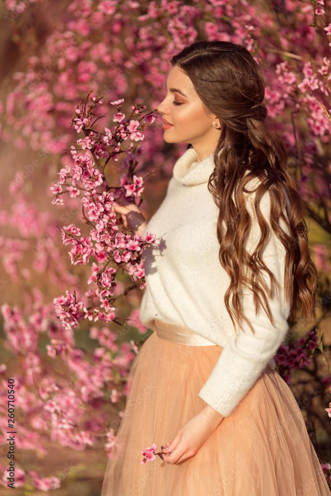 Portrait of young beautiful girl posing near blossom tree with pink flowers.