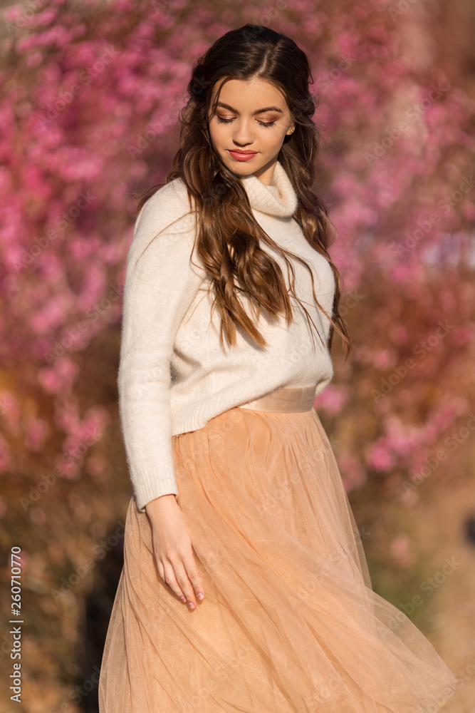 Young beautiful girl with perfect skin is wearing romantic clothes posing near blossom tree in cherry garden Young beautiful girl with perfect skin is wearing romantic clothes posing near blossom tree in cherry garden