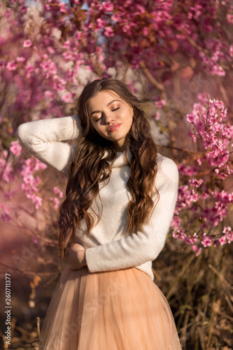 Young beautiful teen girl with perfect skin and makeup is wearing romantic clothes posing near blossom tree in cherry garden