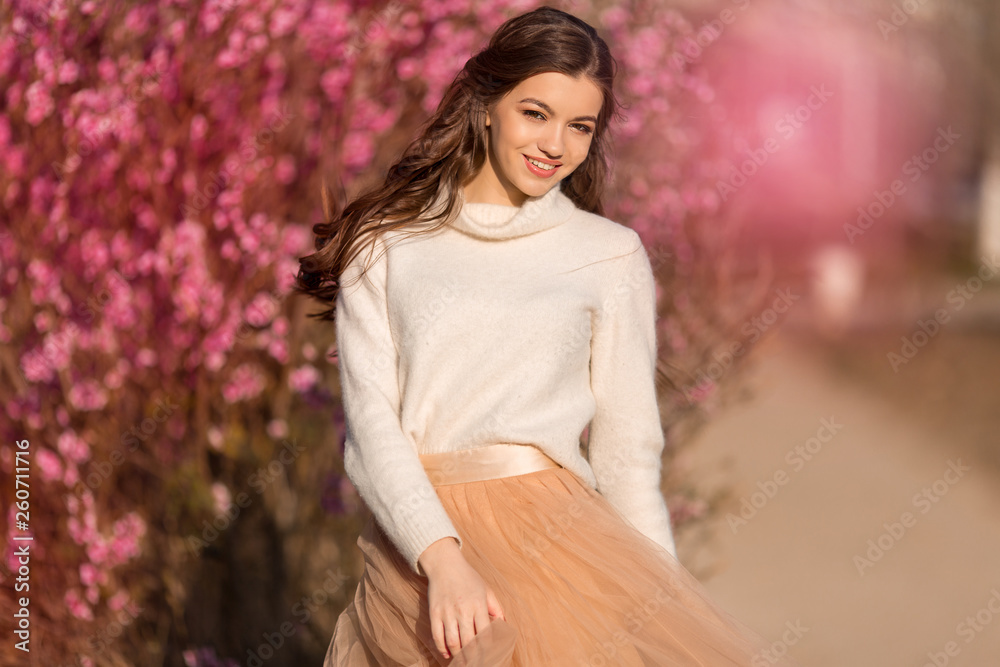 Happy beautiful teen girl with perfect skin and makeup is wearing romantic clothes posing near blossom tree in cherry garden Happy beautiful teen girl with perfect skin and makeup is wearing romantic clothes posing near blossom tree in cherry garden