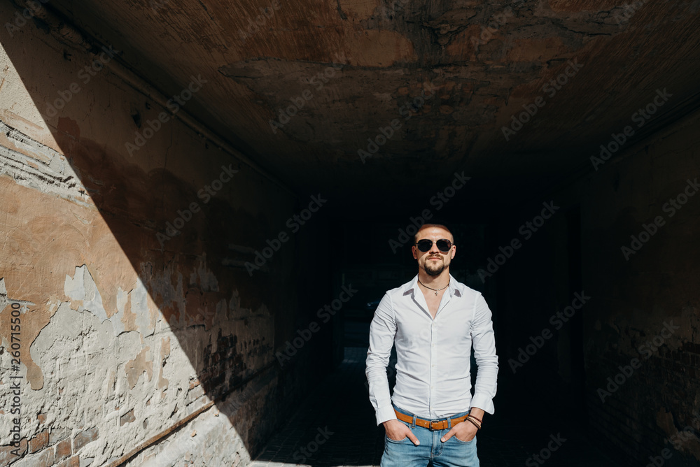 Colorful portrait of a handsome man dressed in white shirt and sunglasses on the grunge background. Happy young man posing outdoor, enjoying the sunny weather.