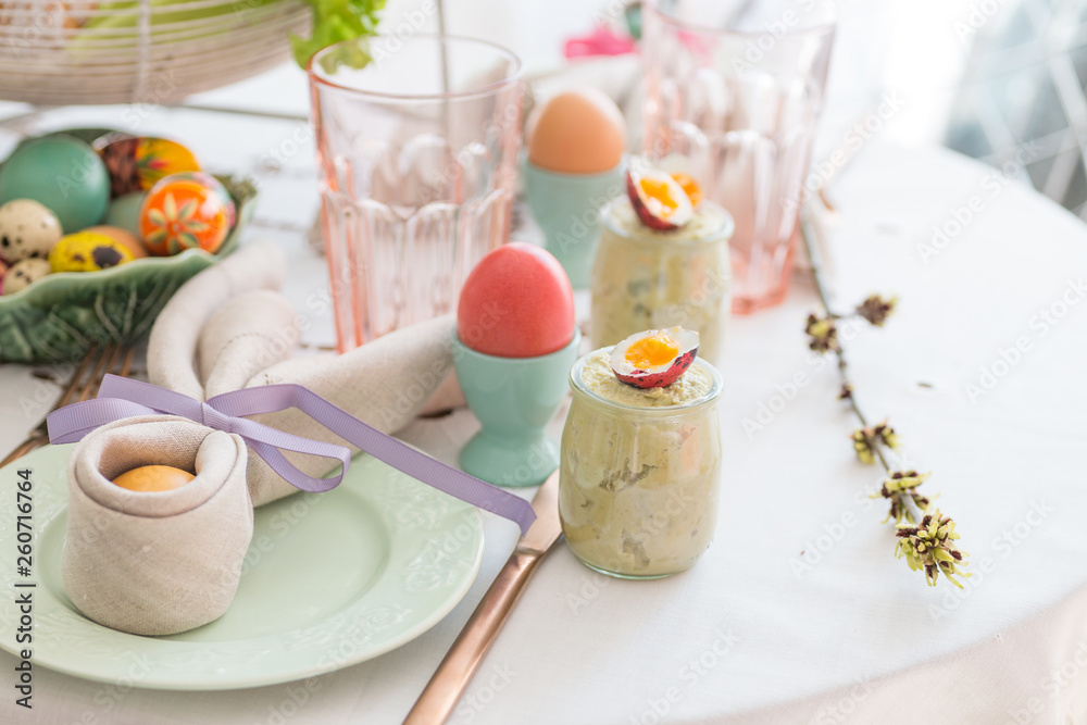 Easter egg wrapped in a linen napkin shaped like bunny ears on Easter breakfast table. Green pea pate in a glass jar with quail egg. Easter egg wrapped in a linen napkin shaped like bunny ears on Easter breakfast table. Green pea pate in a glass jar with quail egg.