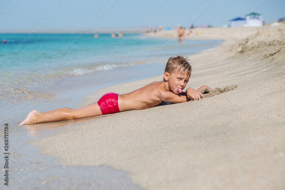 Мальчик на девочке на пляже фото A little boy lying on the sand on the beach is dabbling and showing his tongue ф