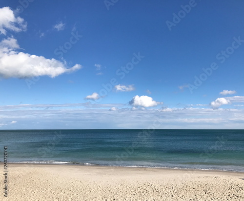 A panorama of a clean sandy shore near the dark blue of the Black Sea against the background of a shallow blue sky.