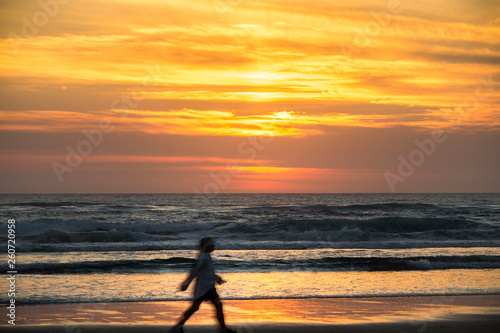 Woman walking on the beach at sunrise