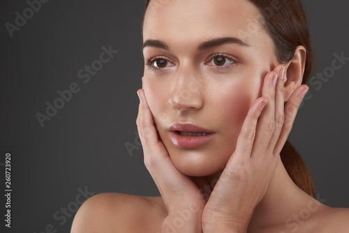 Attractive young woman with natural makeup touching her face