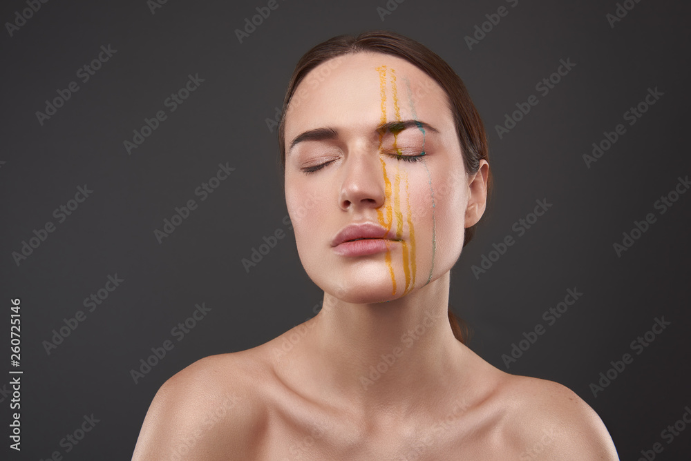 Serene young woman with orange and blue liquid dripping from her face Serene young woman with orange and blue liquid dripping from her face