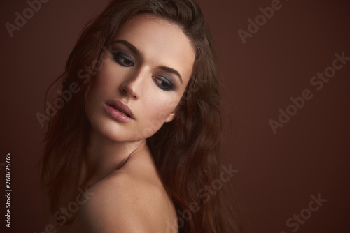 Attractive young woman with evening makeup posing against brown background