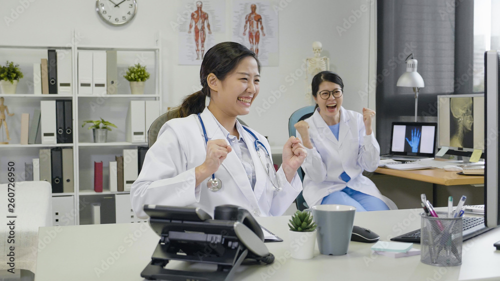 Obraz premium Extremely happy medical professional showing winning sign. female employees joyfully with hands in fist laughing looking computer screen of good news. doctors with success report in hospital office