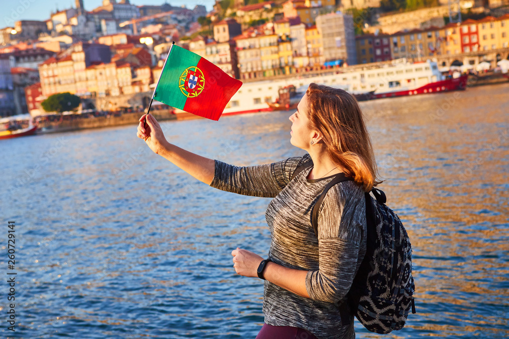 Young woman tourist with portuguese flag enjoying beautiful landscape view on the old town (Ribeira historical quarter) and river Duoro during the sunset in Porto city, Portugal