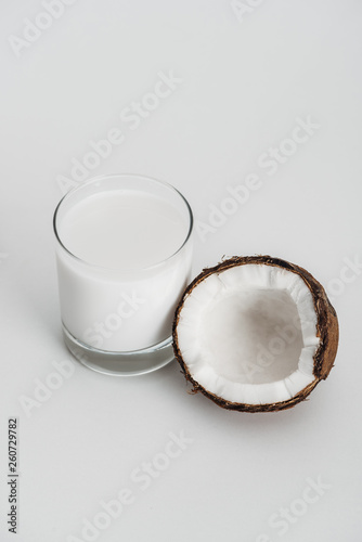 organic vegan coconut milk in glass near coconut half on grey background