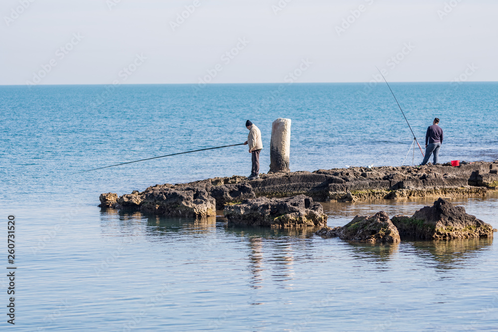 fishermen on the seashore waiting for the catch of the day with their fishing rods