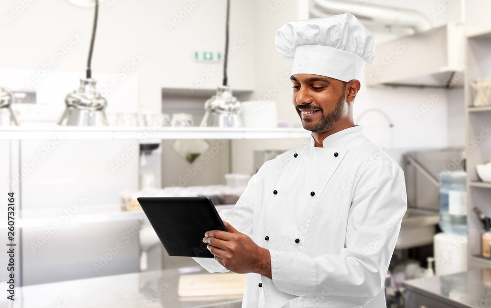 cooking, technology and people concept - happy male indian chef in toque with tablet computer over restaurant kitchen background