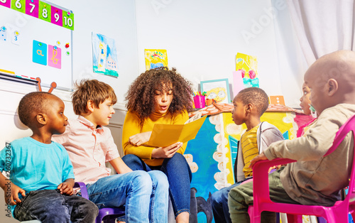 Obraz na plátne Teacher reads a book to group of kids in nursery