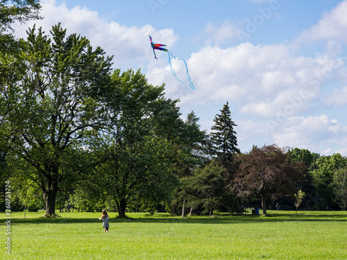 Back view of little girl in light clothes flying a kite in a large park during a summer day, Maisonneuve Park, Montreal, Quebec, Canada photo