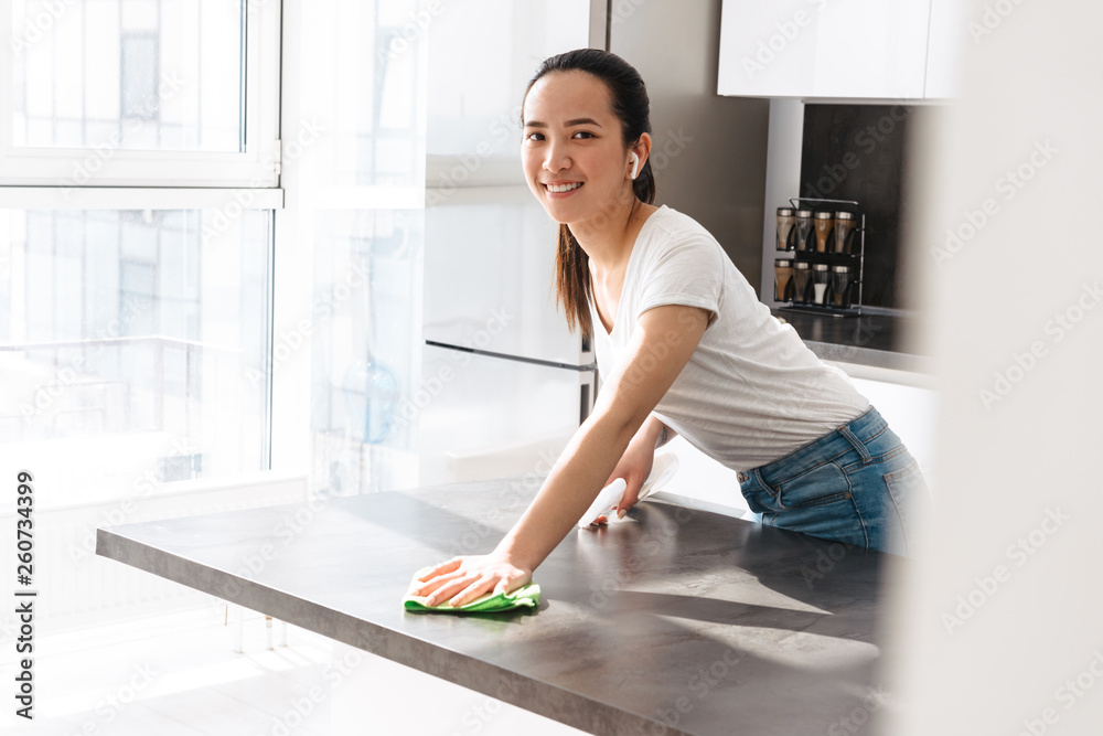 Portrait of pretty asian girl cleaning table with detergent and rag in kitchen at home Portrait of pretty asian girl cleaning table with detergent and rag in kitchen at home