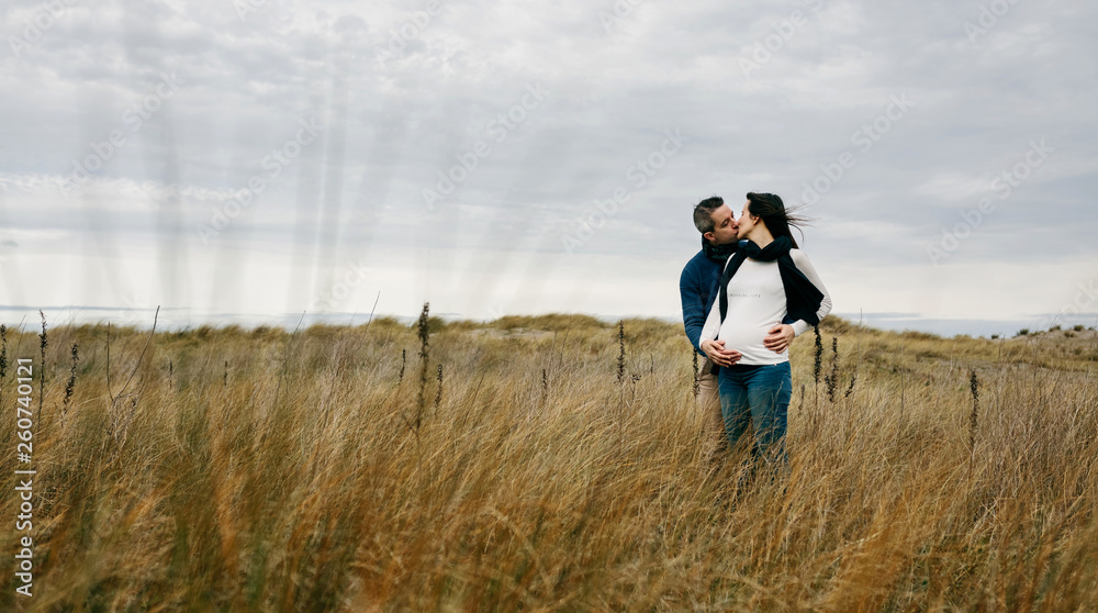 Pregnant with her partner kissing and holding her belly outdoors Pregnant with her partner kissing and holding her belly outdoors