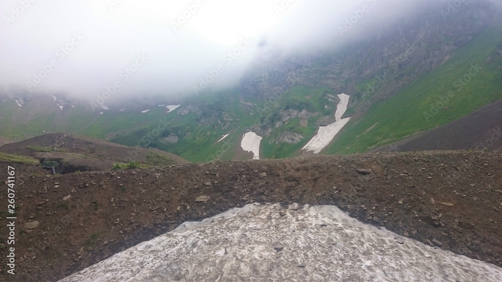 Obraz premium On the slope of a high mountain with a green slope and a top in clouds and fog. Sports and tourist base in the mountains. Krasnaya Polyana, Sochi, Russia.
