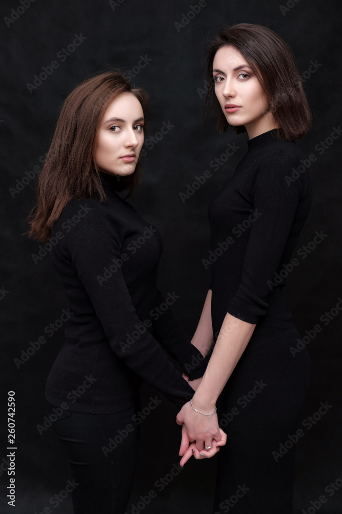Concept portrait of two stylish brunette sisters on a black background in various poses. Fashionable photo of two beautiful girls with dark hair Concept portrait of two stylish brunette sisters on a black background in various poses. Fashionable photo of two beautiful girls with dark hair