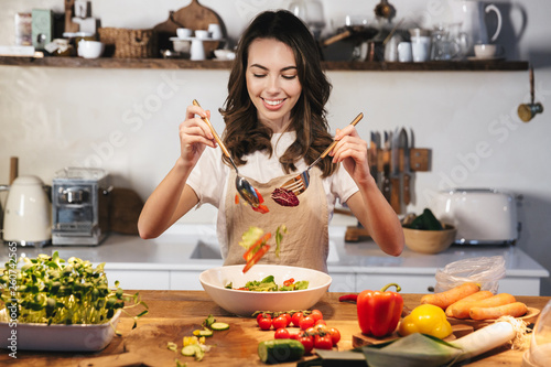 Beautiful young woman wearing apron cooking vegetables