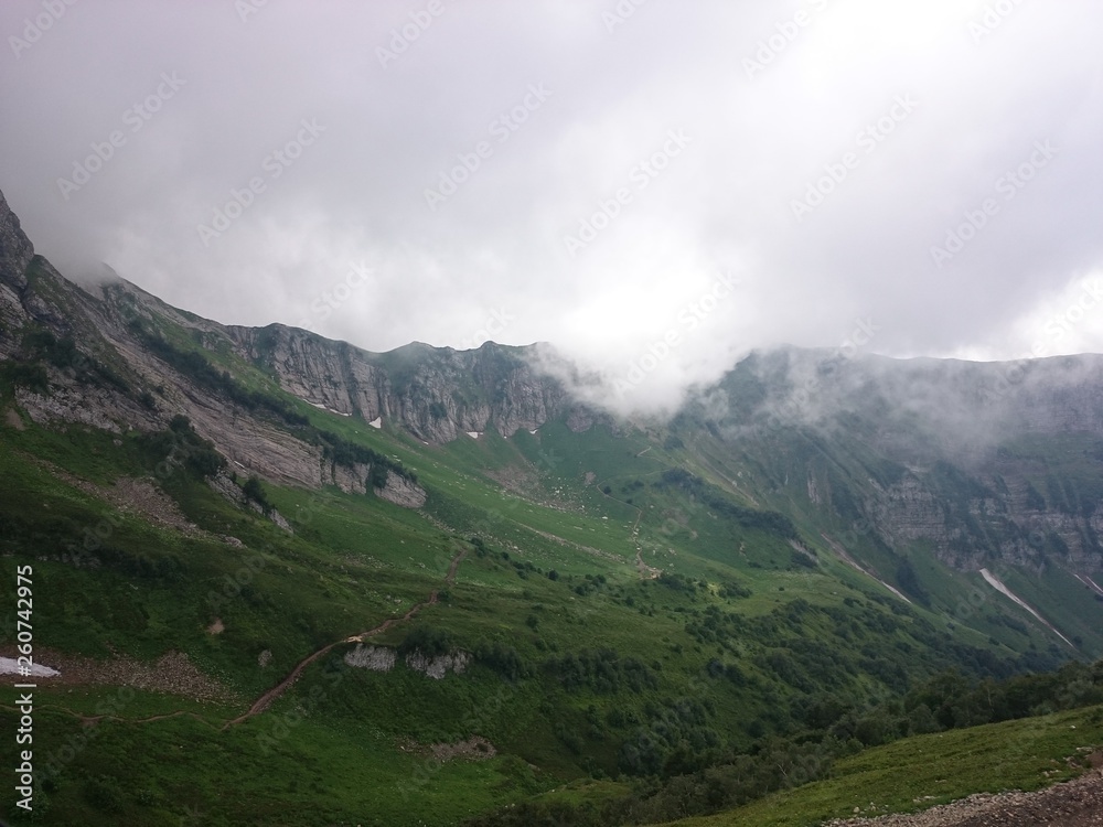 Mountain slope with cable cars and ski slopes on a cloudy summer day, fog, clouds. Black Pyramid Mountain, Krasnaya Polyana, Sochi, Caucasus, Russia.