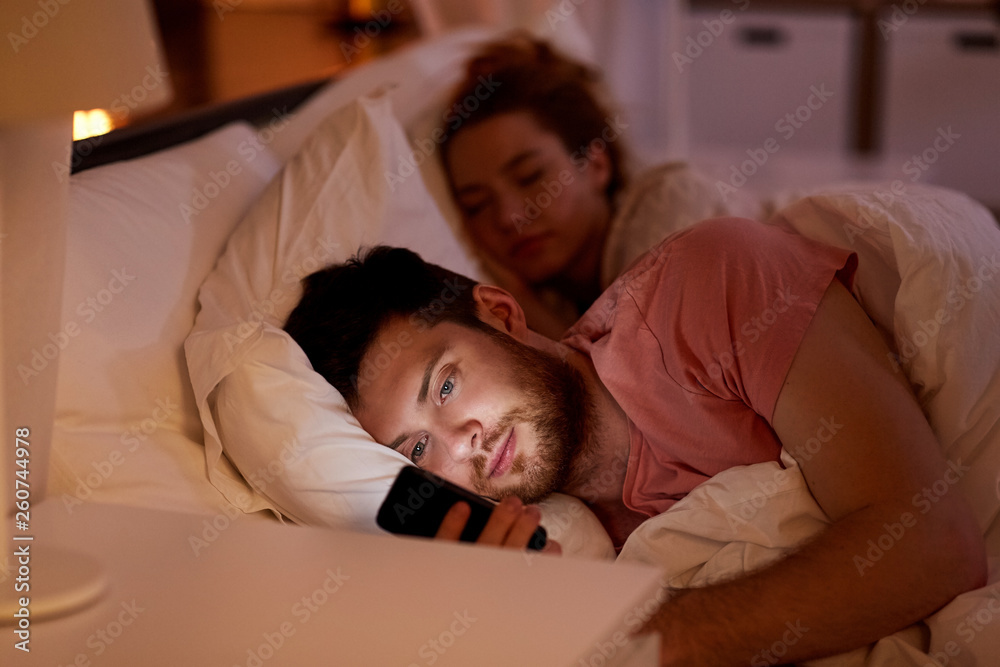 technology, internet addiction and cheat concept - man using smartphone at night while girlfriend is sleeping technology, internet addiction and cheat concept - man using smartphone at night while girlfriend is sleeping