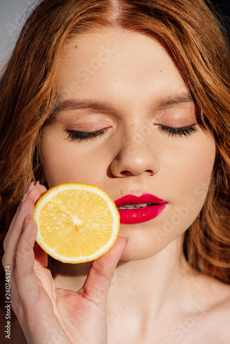 beautiful sensual redhead girl with red lips and eyes closed posing with cut lemon