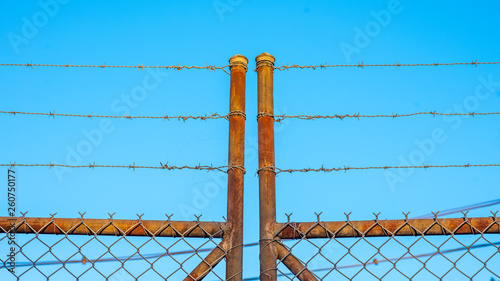 A rusty old barbed wire fence against a blue sky
