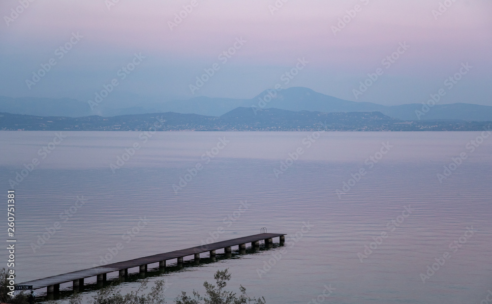 High angle view of Lake Garda with a pier and the mountainous coast on the horizon at sunset, Sirmione, Lombardy, Italy