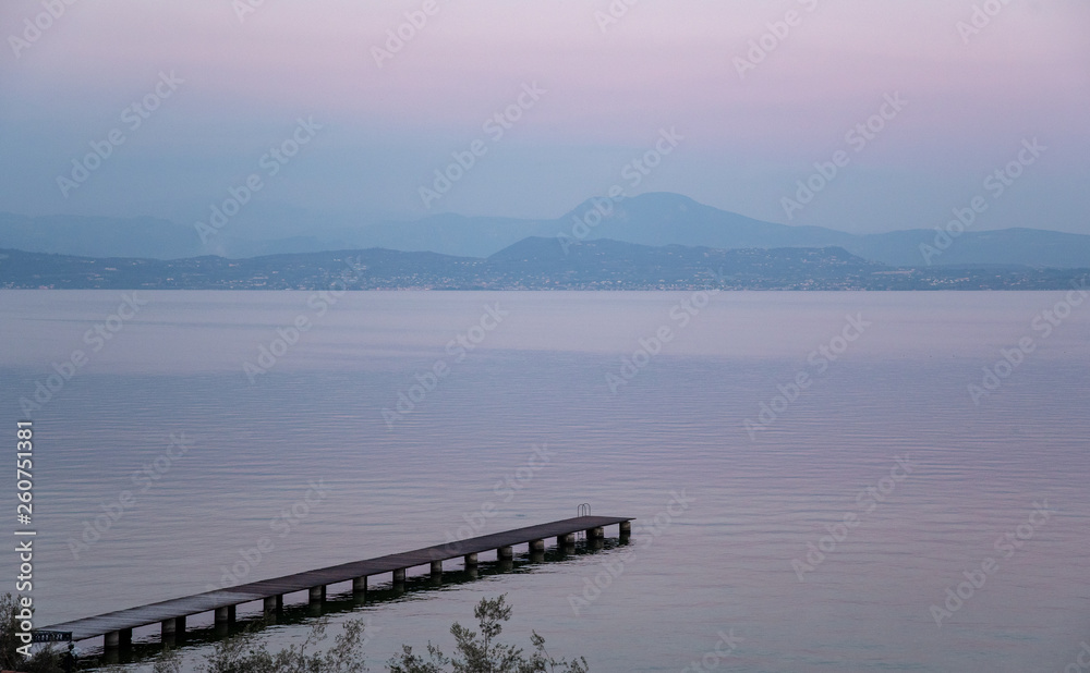High angle view of Lake Garda with a pier and the mountainous coast on the horizon at sunset, Sirmione, Lombardy, Italy High angle view of Lake Garda with a pier and the mountainous coast on the horizon at sunset, Sirmione, Lombardy, Italy