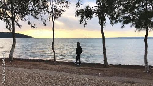 Woman walks on the edge of coast at sunset.