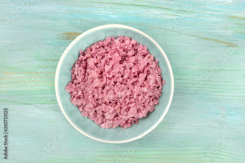 A bowl of pink Himalayan sea salt, shot from the top on a teal blue background with a place for text