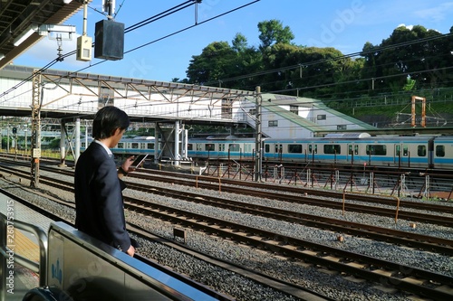 Back view of business man in black suit using mobile phone at train station. People, business, technology, and transportation concept.