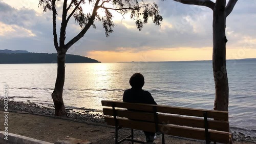 Woman sitting on the bench watching sunset over sea.
