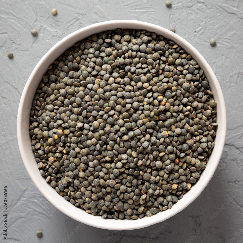 Dry green french lentils in a bowl over gray background, top view. Overhead, from above, flat lay. Dry green french lentils in a bowl over gray background, top view. Overhead, from above, flat lay.