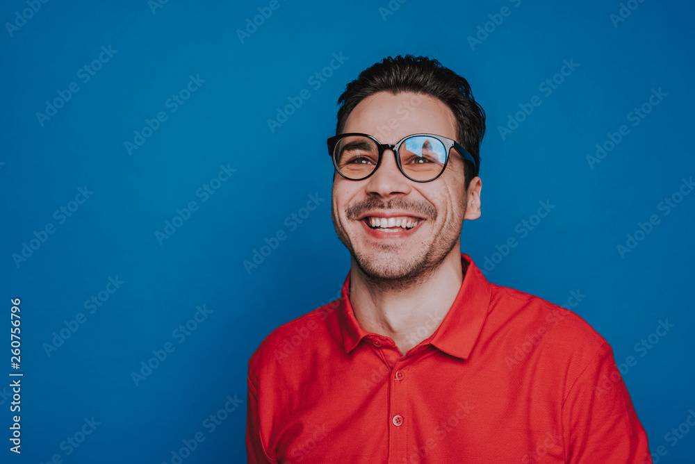 Fototapeta premium Half length of handsome smiling guy in glasses situating on blue background