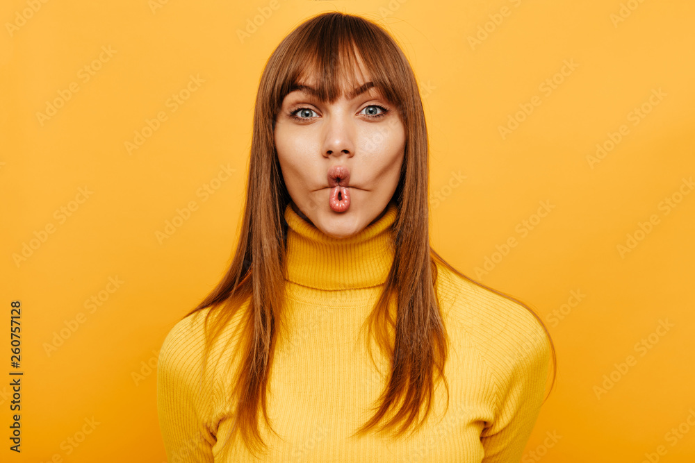 Woman portrait. Fun. Cheerful young woman is grimacing at camera, on a yellow background Woman portrait. Fun. Cheerful young woman is grimacing at camera, on a yellow background