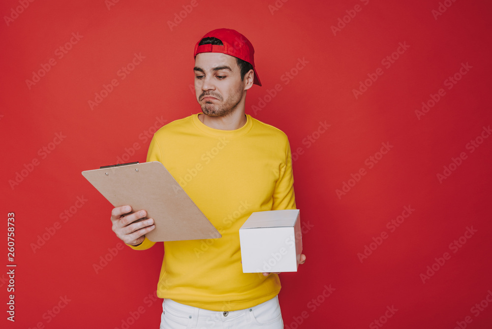 Young guy in cap holding a box and clipboard in arms Young guy in cap holding a box and clipboard in arms