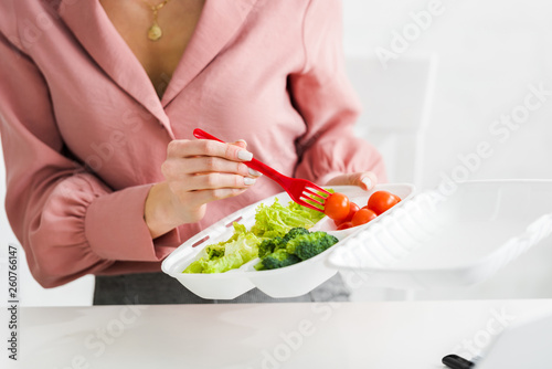 cropped view of woman holding takeaway box with organic vegetables and plastic fork