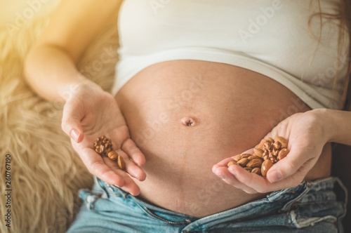 Happy pregnant woman at home eating fresh nuts - almonds, walnuts. Healthy pregnancy concept.