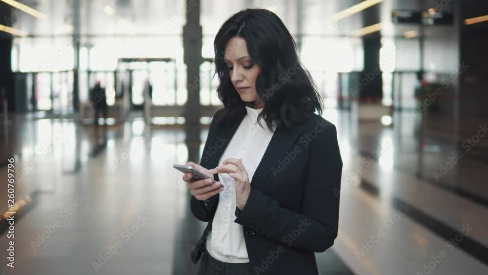 Young woman texting on a mobile phone while standing in the lobby of a modern office building. Young woman texting on a mobile phone while standing in the lobby of a modern office building.
