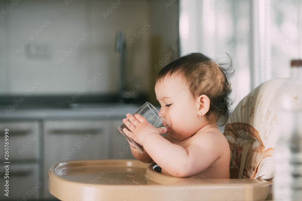 Cute little girl sitting in baby chair and drinking water Cute little girl sitting in baby chair and drinking water