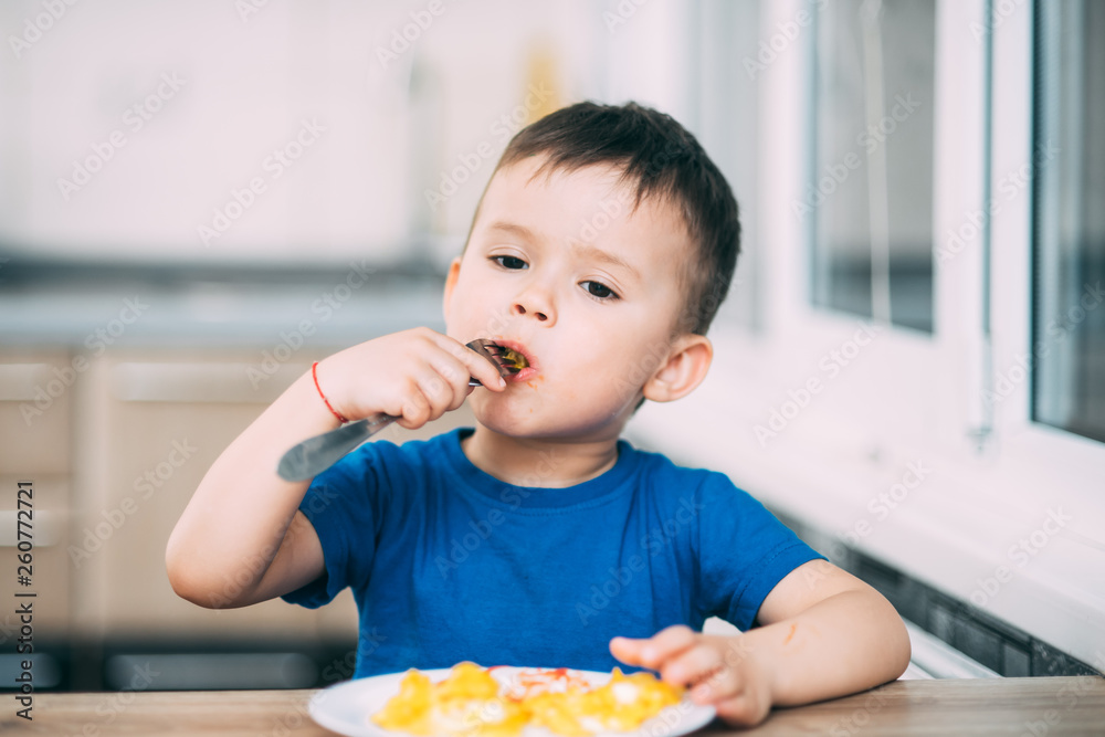a child in a t-shirt in the kitchen eating an omelet, a fork a child in a t-shirt in the kitchen eating an omelet, a fork