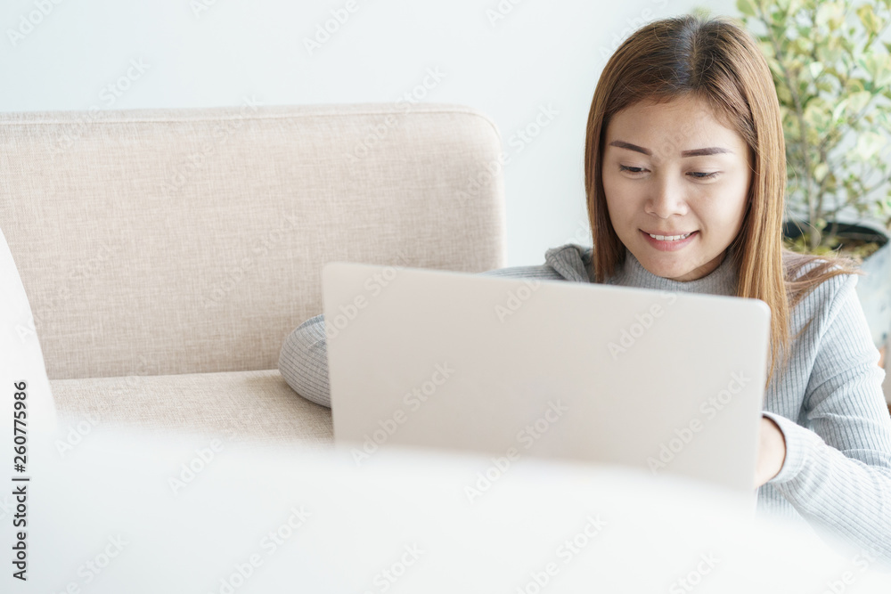Asian woman is working on a laptop in the living room. She sit on the floor and sofa is office desk. Asian woman is working on a laptop in the living room. She sit on the floor and sofa is office desk.