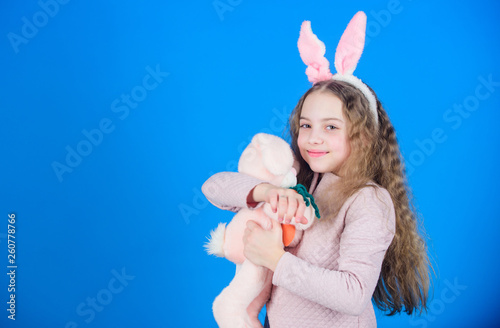 Cute and adorable. Bunny girl with cute toy on blue background. Child smiling play bunny toy. Happy childhood. Get in easter spirit. Bunny ears accessory. Lovely playful bunny child with long hair