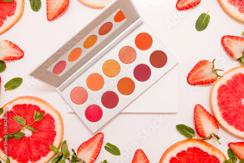 Fototapeta Naklejka Na Ścianę i Meble -  Cute flat lay with palette of cosmetics with fresh fruit, cut strawberries and grapefruit or red orange, mint leaves