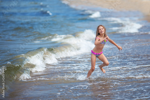 Cute little girl runing along the seashore against a clear blue sky and rejoices in the rays of the summer sun