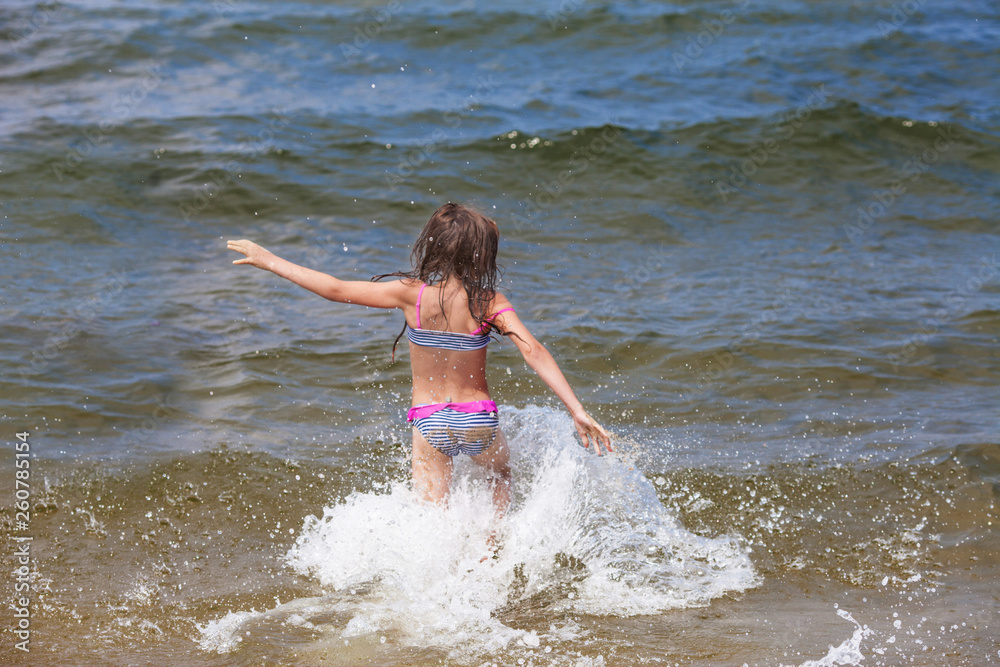 Little girl runing in the sea. View from a back